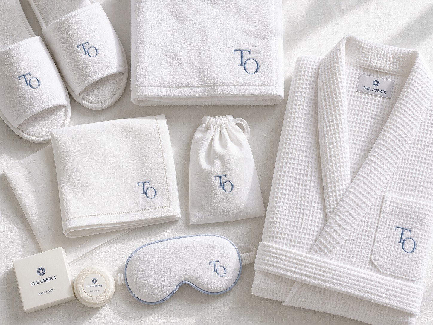 A flat-lay of white linen items embroidered with a hotel monogram in pale blue thread